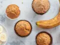 Leckere Bananen Muffins, frisch gebacken, mit einer reifen Banane und Bananenscheiben daneben.