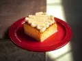 Ein Stück saftiger Tres Leches Kuchen mit Sahnetupfern auf einem roten Teller, bereit zum Genießen.