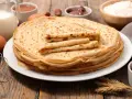 Ein Stapel goldbrauner Pfannkuchen, zubereitet nach einem sehr guten Pfannkuchen Rezept, daneben Zutaten wie Milch, Eier, Mehl, Marmelade und Nuss-Nougat-Creme.
