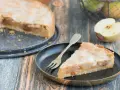 Ein Stück von einem köstlichen, gedeckten Apfelkuchen mit Zuckerguss und Mandelsplittern auf einem Teller. Daneben ein halber Apfel.