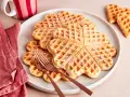 Herzförmige Waffeln, bestäubt mit Puderzucker. Ein köstlicher waffelteig ohne butter, serviert auf einem Teller mit zwei Gabeln.