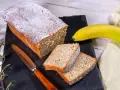 Saftiger Bananenkuchen, bestäubt mit Puderzucker, neben einer Banane und einem Messer. Perfekt für ein Bananenkuchen Rezept.