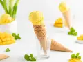 Ein Stapel Waffelkegel mit cremigem Mango Eis, garniert mit frischer Minze und Mangostücken. Ein süßer Genuss!