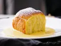 Ein goldbraunes Buchtel, mit Puderzucker bestäubt, ruht in einer cremigen Vanillesauce. Ein köstliches Buchtel Rezept zum Nachbacken.