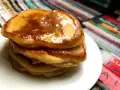 Ein Stapel goldbrauner Pancakes mit Kefir, beträufelt mit Honig, auf einem weißen Teller.
