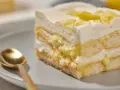 Ein Stück Zitronen Tiramisu mit cremiger Füllung und Zitronenscheiben, daneben eine goldene Löffel.