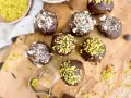 Selbstgemachte Pralinen mit Schokolade und gehackten Nüssen, einige mit Pistazien bestreut. Ein Herz-Ausstecher liegt daneben.