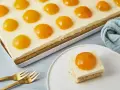 Ein rechteckiger Kuchen mit einer cremigen Schicht und vielen Pfirsichhälften, die wie ein Spiegelei Kuchen aussehen. Ein Stück auf einem Teller daneben.