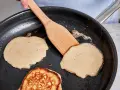 Buttermilch pancakes braten in der Pfanne. Ein Holzspatel wendet einen goldbraunen Pancake.