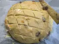 Ein runder Teigling mit eingeschnittenen Rauten, bereit für das Osterfladen Rezept. Rosinen und Orangenschale sind sichtbar.