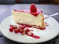 Ein Stück cremiger Käsekuchen mit Himbeersoße und frischen Beeren, bestäubt mit Puderzucker. Ein Genuss für alle Sinne, diese Himbeer Torte.
