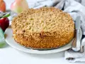 Ein goldbrauner Haferflocken Kuchen mit knuspriger Kruste, daneben Äpfel und ein Messer.