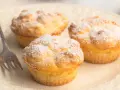 Drei luftige cheesecake muffins, bestäubt mit Puderzucker, warten auf einer Platte auf eine Gabel.