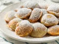 Ein Teller voller goldbrauner Poffertjes, bestäubt mit Puderzucker. Dieses Poffertjes Rezept ist ein Genuss!