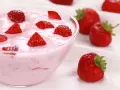 Ein cremiges Erdbeer Dessert in einer Schüssel, garniert mit frischen Erdbeerstücken. Daneben liegen ganze Erdbeeren.