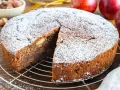 Ein saftiger russischer Apfelkuchen, bestäubt mit Puderzucker, wartet auf seine Genießer. Apfelstücke sind im dunklen Teig sichtbar.