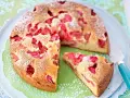 Ein saftiger Erdbeer Rhabarber Kuchen, bestäubt mit Puderzucker, liegt auf einem Teller. Ein Stück wurde bereits entnommen.