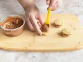 Hände belegen Kekse mit Nutella. Leckere Nutella Kekse entstehen auf dem Holzbrett.
