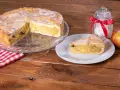 Omas weltbester Apfelkuchen, saftig und mit Zuckerguss überzogen, wartet auf einem Tortenständer. Ein Stück auf einem Teller und ein Apfel daneben laden zum Genießen ein.
