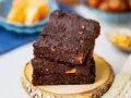 Gestapelte, saftige vegane Brownies mit Nüssen, auf einem Holzscheit.