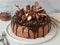 Eine üppige Nutella Torte, dekoriert mit vielen Schokoriegeln und Pralinen, daneben ein Glas Nutella.