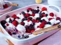Ein cremiges Windbeutel-Dessert mit frischen Beeren wie Himbeeren, Brombeeren und Blaubeeren, serviert in einer rosa Schale.