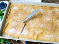 Ein frisch gebackener Ofenpfannkuchen, bestreut mit Zucker und Zimt, bereit zum Servieren. Ein Stück wird mit einem Löffel herausgehoben.