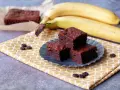 Saftige Bananen Brownies auf einem gelben Tuch, daneben reife Bananen. Ein Genuss!
