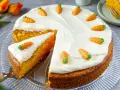 Saftiger Karottenkuchen mit cremigem Frosting und süßen Marzipan-Karotten. Ein Stück ist bereits angeschnitten.