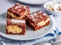 Drei Stücke saftiger Schoko Kokos Kuchen mit Schokoladenglasur und Kokosraspeln auf einem grauen Teller.