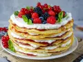 Eine hohe Pfannkuchen Torte mit Sahne und roter Marmelade, gekrönt mit frischen Beeren und Minze.