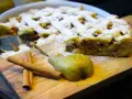 Ein köstlicher Birnenkuchen mit Gittermuster, bestäubt mit Puderzucker. Daneben liegen eine Birne und Zimtstangen – perfekt für ein Birnenkuchen Rezept.