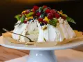 Ein köstliches Pavlova-Rezept mit frischen Beeren, Kiwi und Passionsfrucht. Ein Stück ist bereits angeschnitten.