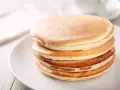 Ein Stapel goldbrauner, glutenfreier Pfannkuchen auf einem weißen Teller, bereit zum Genießen.