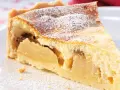 Ein Stück saftiger Apfelkuchen mit Quark, bestäubt mit Puderzucker, auf einem weißen Teller.
