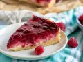 Ein saftiges Stück Himbeer Schmand Kuchen mit frischen Himbeeren und glänzender Glasur auf einem Teller.