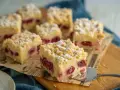 Saftiger Kirschkuchen mit Pudding und Streuseln, bestäubt mit Puderzucker. Ein Stück wird gerade serviert.