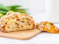 Ein goldbraunes Osterbrot mit Mandelsplittern und Rosinen, perfekt für Ihr Osterbrot Rezept. Daneben ein Stück des süßen Gebäcks.