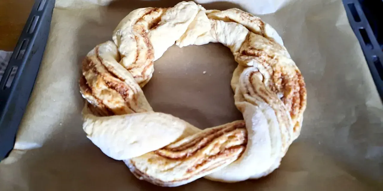 Ein geflochtener Teigring mit Zimtfüllung liegt auf Backpapier. Perfekt für das Osterkranz backen.