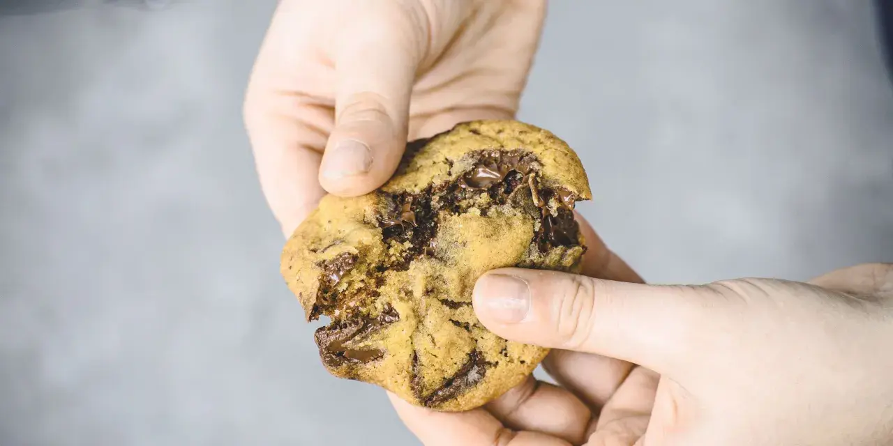 Hände halten einen zerkrümelten Schokoladenkeks, der nach einem einfachen Cookies Rezept gemacht wurde.