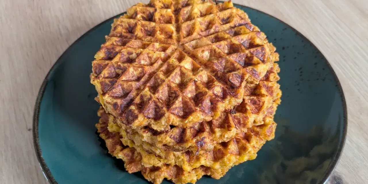 Ein Stapel goldbrauner Haferflocken Waffeln auf einem dunklen Teller. Sie sehen knusprig und lecker aus, perfekt für ein gesundes Frühstück.