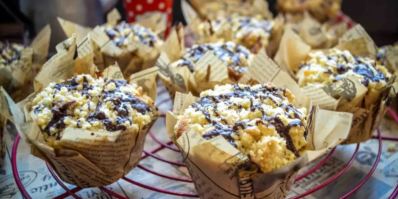 Saftige Nutella Muffins mit Streuseln und Schokoglasur, verpackt in Zeitungspapier-Förmchen, auf einem roten Gitter.