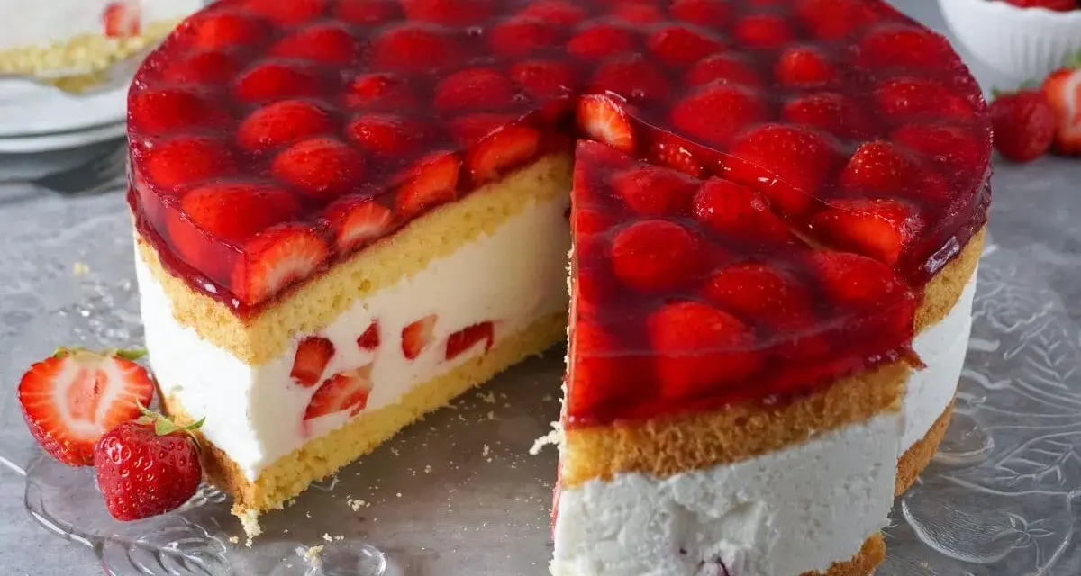 Eine saftige Erdbeer Sahne Torte mit frischen Erdbeeren und Tortenguss, ein Stück ist bereits angeschnitten.