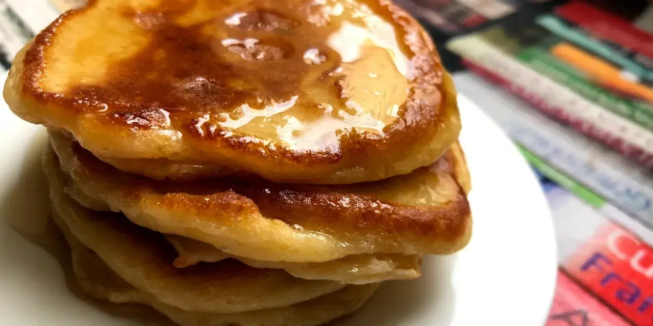 Ein Stapel goldbrauner Pancakes mit Kefir, beträufelt mit Honig, auf einem weißen Teller.