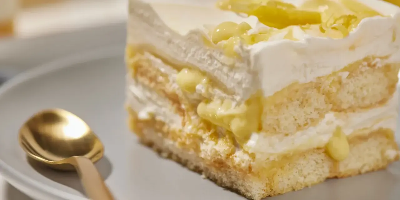 Ein Stück Zitronen Tiramisu mit cremiger Füllung und Zitronenscheiben, daneben eine goldene Löffel.