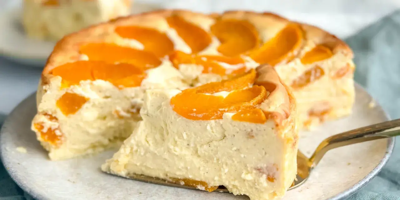 Ein saftiger Pfirsichkuchen mit cremiger Füllung und frischen Pfirsichspalten. Ein Stück wird gerade mit einem goldenen Tortenheber herausgehoben.