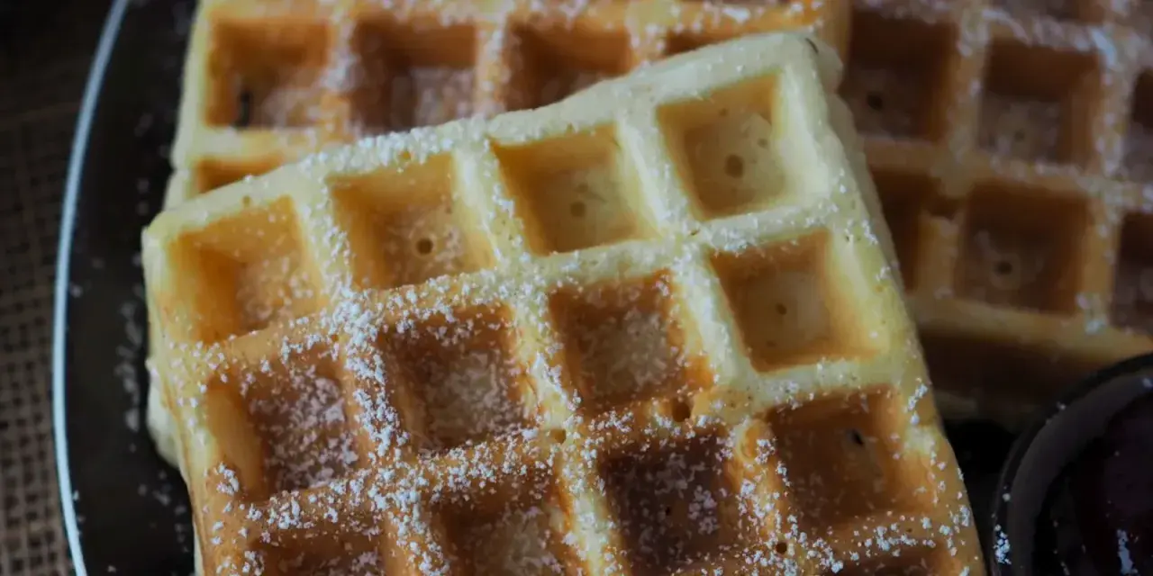 Goldbraune Waffeln, bestäubt mit Puderzucker, warten auf Joghurt. Ein süßer Genuss!