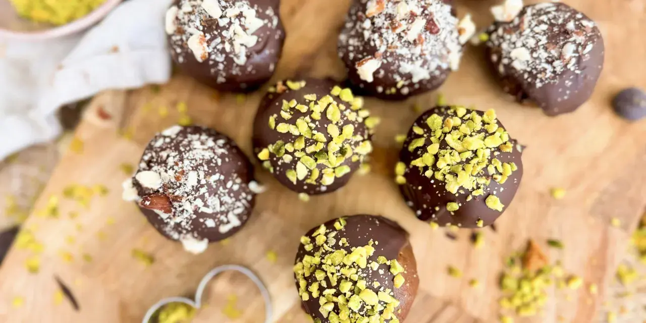 Selbstgemachte Pralinen mit Schokolade und gehackten Nüssen, einige mit Pistazien bestreut. Ein Herz-Ausstecher liegt daneben.