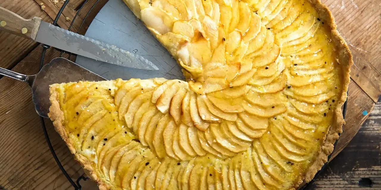 Ein köstliches Apfeltarte Rezept mit dünn geschnittenen Äpfeln, die wie Fächer angeordnet sind. Ein Stück wurde bereits herausgeschnitten.
