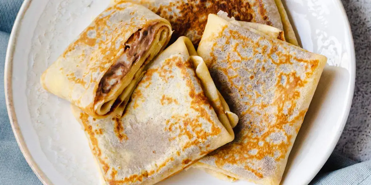 Gefaltete Crêpes mit Schokoladencreme-Füllung, ein köstliches Crepes Rezept, liegen auf einem Teller.